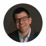 Smiling man in glasses wearing a dark blazer over a collared shirt, professional headshot for business networking and leadership profiles.