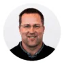 Middle-aged Caucasian male in glasses smiling at the camera, wearing a black polo shirt, professional headshot for business profile.